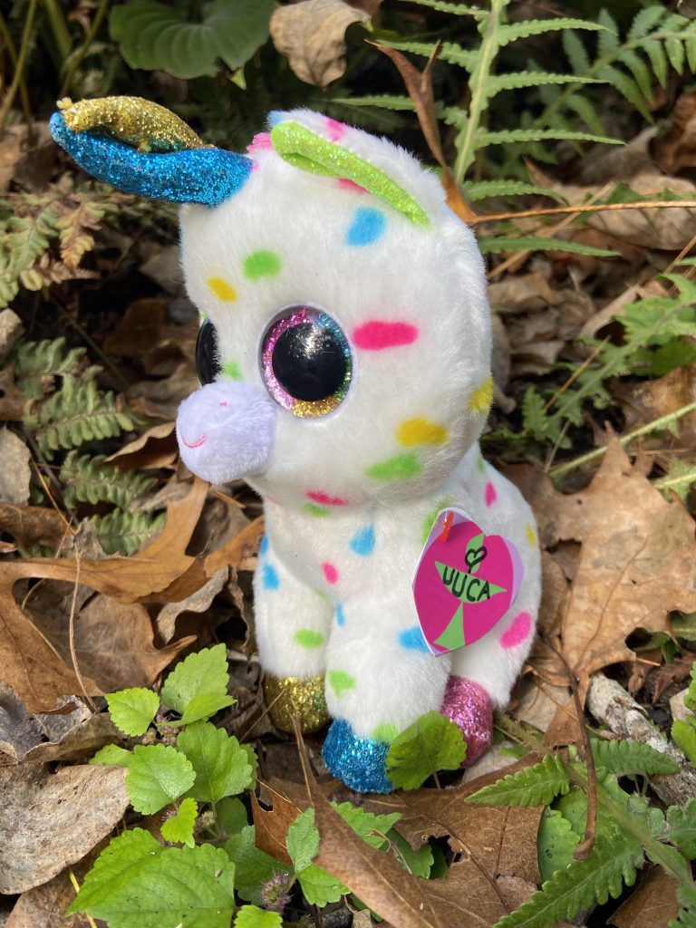 white plush unicorn with mlti-colred spots sitting in garden